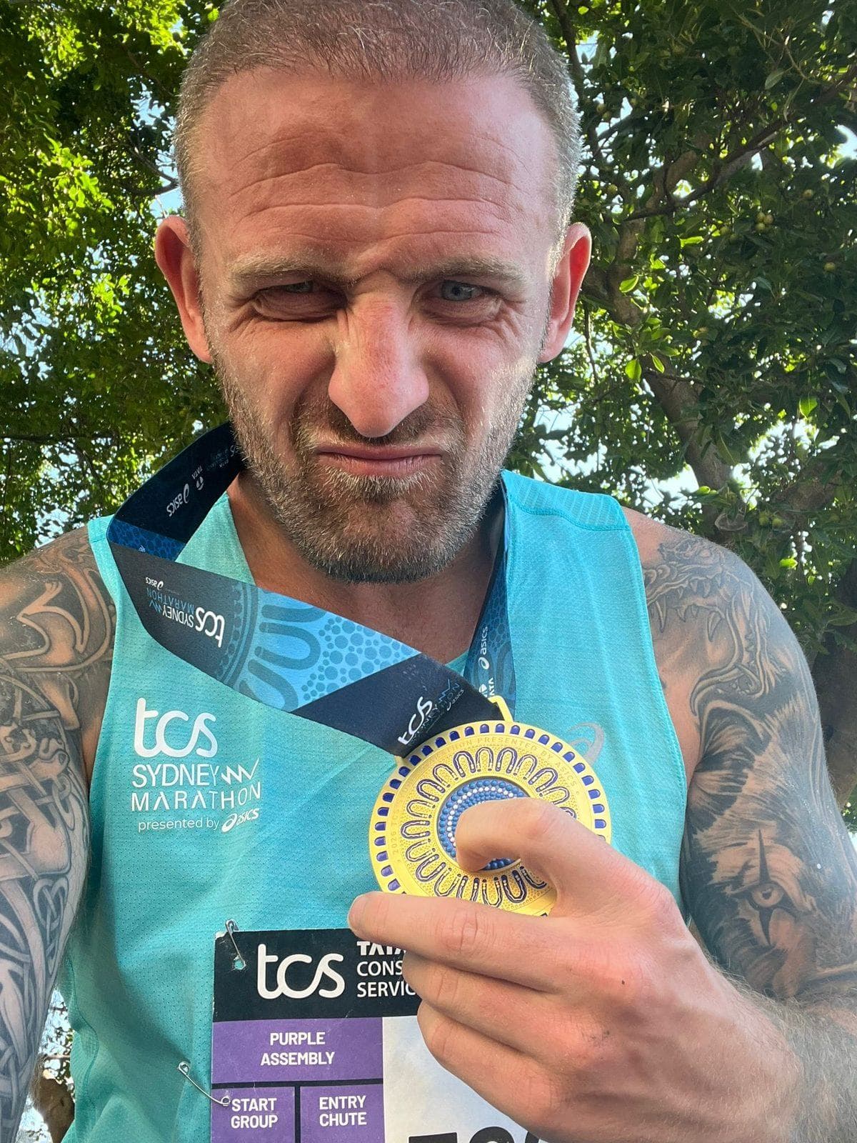 Denny holding up the Sydney Marathon 2026 finisher medal
